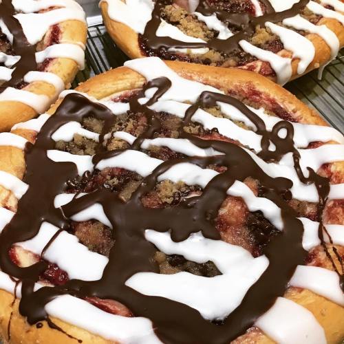 Freshly baked cinnamon rolls drizzled with chocolate and topped with cream and crumbly filling.