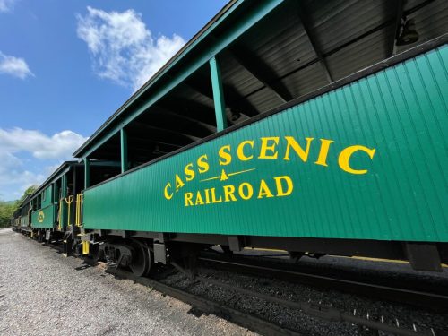 Green train car with "Cass Scenic Railroad" painted in yellow, under a blue sky with scattered clouds.