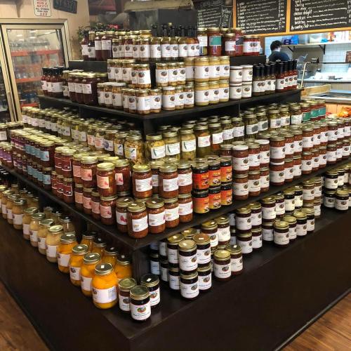 A display of various jars and bottles of sauces, jams, and preserves arranged on shelves in a store.