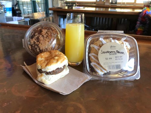 A breakfast spread featuring a biscuit sandwich, pecan scone, coffee cake, and a glass of orange juice on a table.