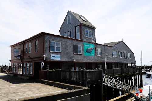 A waterfront building with a wooden deck, featuring multiple stories and signs, set against a clear sky.