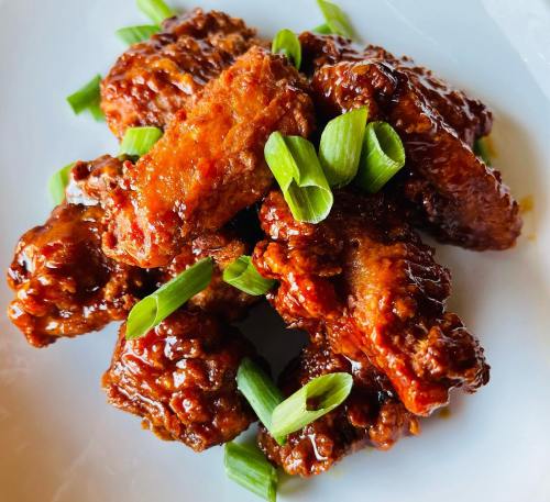A plate of glazed chicken wings garnished with chopped green onions.