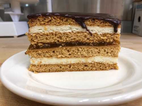 A slice of layered cake with a chocolate glaze, featuring cream and caramel layers on a white plate.