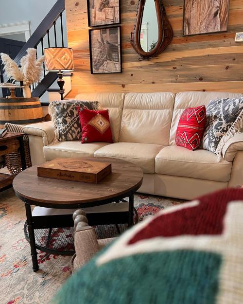 Cozy living room with a beige sofa, decorative pillows, wooden accents, and a round coffee table on a patterned rug.