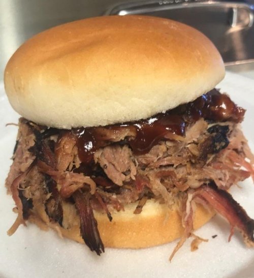 A close-up of a pulled pork sandwich topped with barbecue sauce on a soft bun.