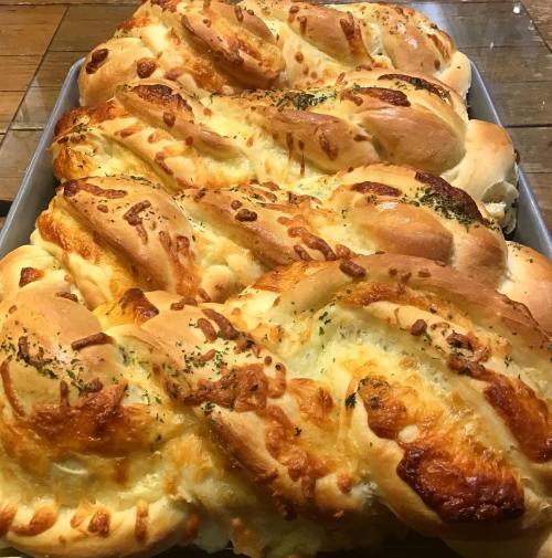 A tray of freshly baked, golden-brown braided bread topped with cheese and herbs.