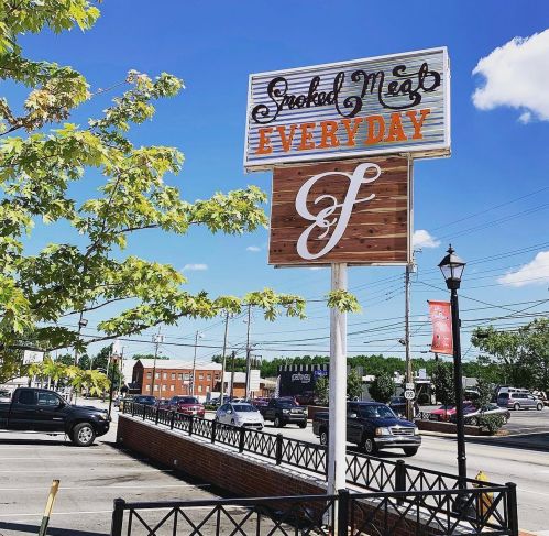 Sign for "Grilled Meat Everyday" with a blue sky and trees in the foreground, located on a busy street.