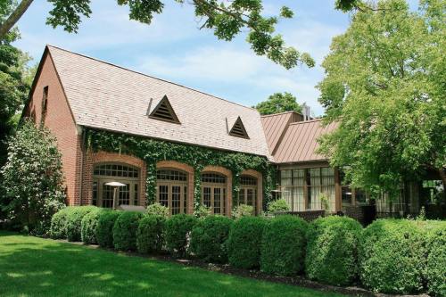 A charming brick building with a sloped roof, surrounded by lush greenery and neatly trimmed hedges under a clear blue sky.