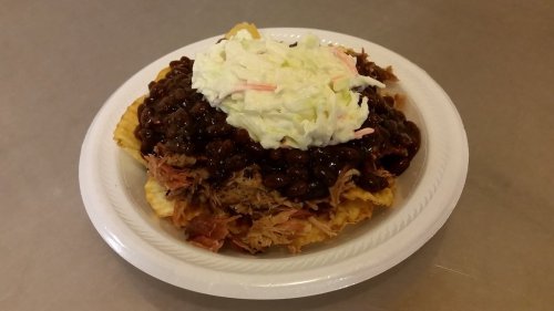 A plate of nachos topped with shredded meat, black beans, and a dollop of coleslaw.