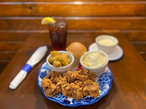 A plate of fried chicken with sides of okra, mashed potatoes, a roll, and a glass of iced tea on a wooden table.