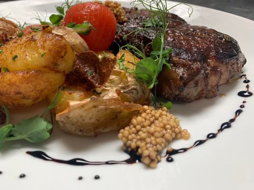 A gourmet plate featuring grilled steak, roasted potatoes, cherry tomatoes, and mustard seeds, garnished with herbs.