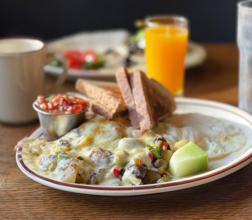 A plate of cheesy breakfast with eggs, potatoes, salsa, and toast, accompanied by a glass of orange juice.