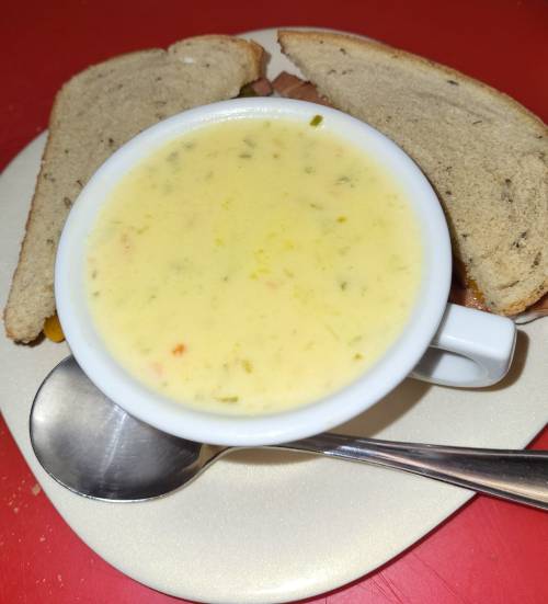 A small cup of creamy soup on a plate, accompanied by two slices of bread. A spoon rests beside the cup.