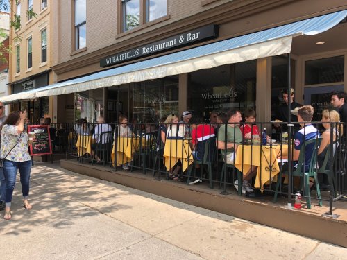 Outdoor dining scene at Wheatfields Restaurant & Bar, with patrons seated at tables under a canopy.