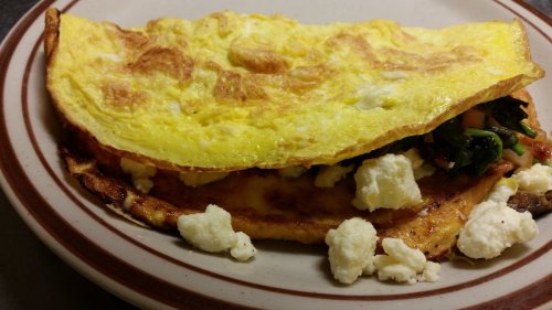 A fluffy omelette filled with spinach, tomatoes, and topped with crumbled cheese, served on a plate.