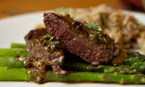 A close-up of tender steak slices on a bed of asparagus, drizzled with a rich sauce, served with a side of rice.