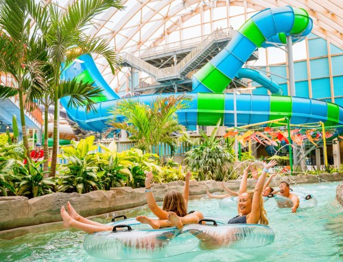 People enjoying a lazy river ride in a tropical indoor water park with a large water slide in the background.