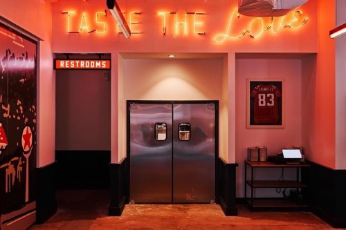 A vibrant interior with a neon sign reading "TASTE THE LOVE," metal doors, and a restroom sign in a stylish setting.