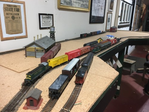 A model train layout featuring various colorful train cars and a station on a wooden table in a room with framed pictures.