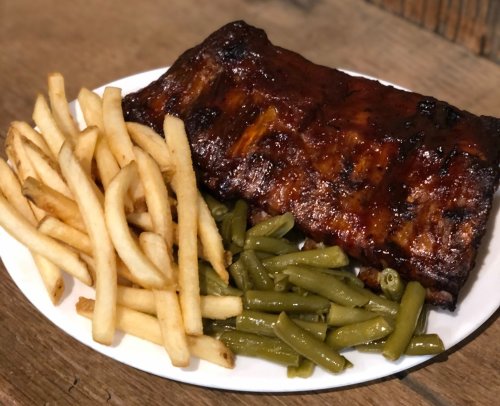 A plate of barbecue ribs with a side of green beans and French fries.