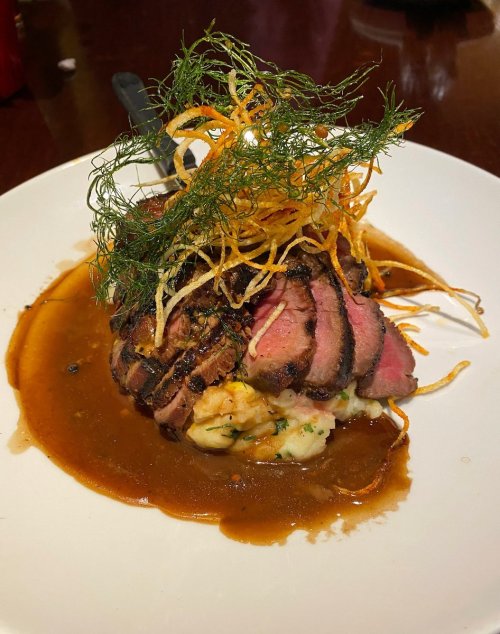 A beautifully plated dish featuring sliced meat topped with crispy onions and herbs, served on a rich sauce.