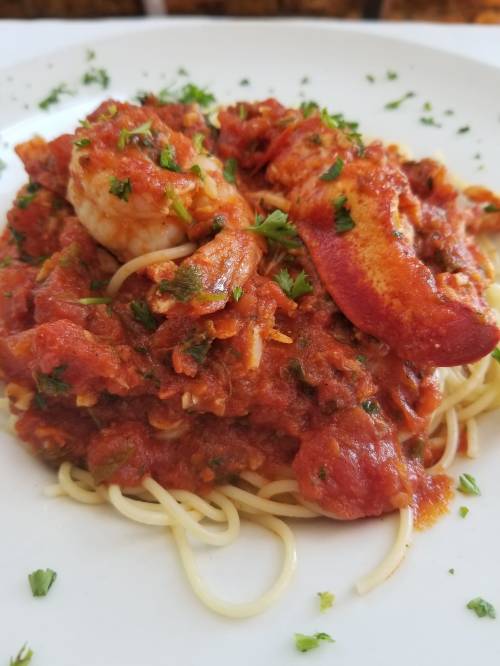 A plate of spaghetti topped with lobster and shrimp in a rich tomato sauce, garnished with parsley.