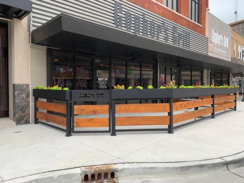 Outdoor dining area with wooden and metal barriers, featuring colorful flowers, outside a restaurant.