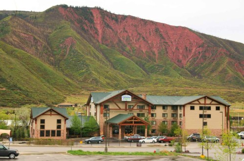 A hotel building in front of a lush green mountain with reddish rock formations in the background.