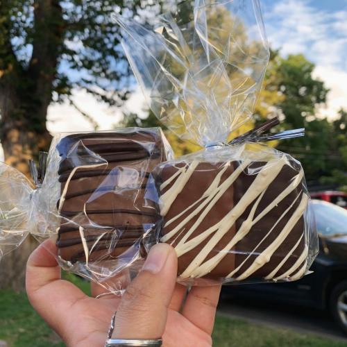 A hand holding two chocolate treats wrapped in clear plastic, with one drizzled in white chocolate.