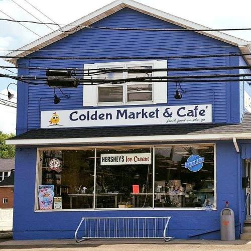 A blue building with a sign reading "Colden Market & Café," featuring a window display with ice cream and snacks.
