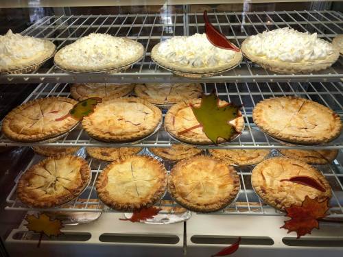 A display case filled with various pies, including cream pies and fruit pies, decorated with autumn leaves.