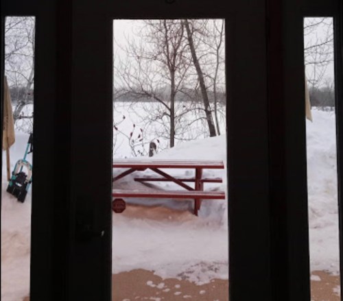 View through a doorway showing a snowy landscape with a picnic table and bare trees in the background.