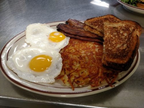 A plate of breakfast featuring two fried eggs, crispy bacon, hash browns, and toasted bread.