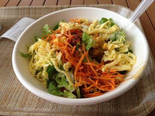 A bowl of mixed salad with shredded lettuce, carrots, and corn, served with a plastic fork on a tray.