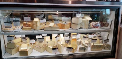 A display case filled with various types of cheese, each labeled with names and descriptions.