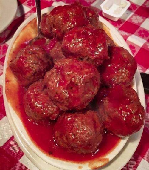 A plate of large meatballs covered in rich red sauce, served on a checkered tablecloth.