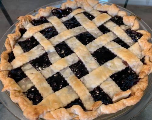 A freshly baked blueberry pie with a golden lattice crust, sitting in a glass pie dish.