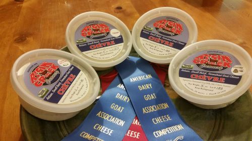 Four containers of goat cheese labeled "Chevre" on a plate, accompanied by blue ribbons from a cheese competition.