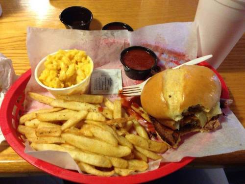 A basket with a sandwich, fries, macaroni and cheese, and dipping sauces on a wooden table.