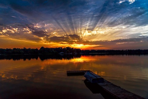 A serene lake at sunset, with vibrant clouds and rays of light reflecting on the water's surface.