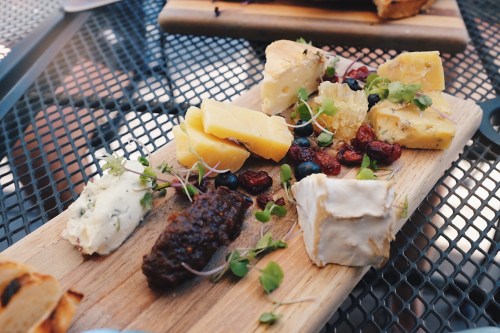 A wooden cheese board featuring various cheeses, dried fruits, and garnishes on a textured black table.