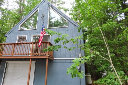 A blue house with large windows and a wooden deck, surrounded by trees, featuring an American flag hanging outside.