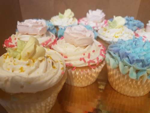 A variety of decorated cupcakes with colorful frosting and floral designs, arranged in a box.
