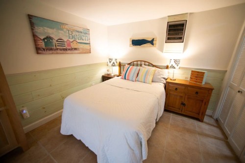 Cozy bedroom with a double bed, beach-themed decor, wooden furniture, and soft lighting.