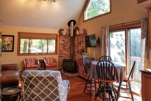 Cozy living room with a wood stove, large windows, and a dining table, featuring warm colors and comfortable seating.