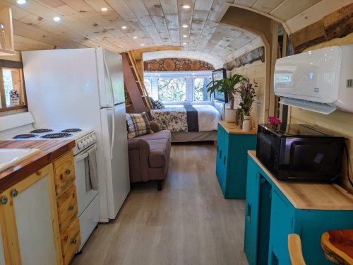 Cozy interior of a tiny home on wheels, featuring a kitchen, living area, and a bedroom with large windows.