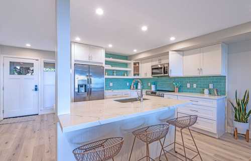 Modern kitchen with white cabinets, turquoise backsplash, stainless steel appliances, and a large island with bar stools.