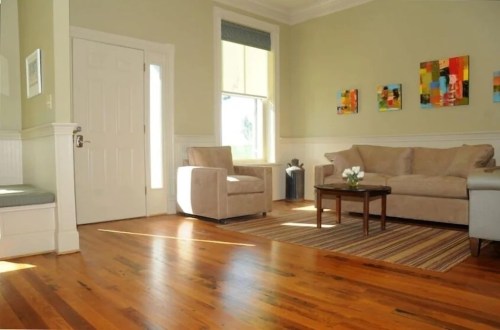 Bright living room with light green walls, hardwood floors, a beige sofa, a coffee table, and colorful wall art.