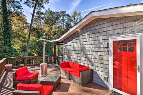 A cozy outdoor patio with red furniture, a glass table, and a red door, surrounded by trees and greenery.