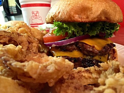A close-up of a cheeseburger with lettuce, tomato, and onion, served with crispy onion rings on the side.